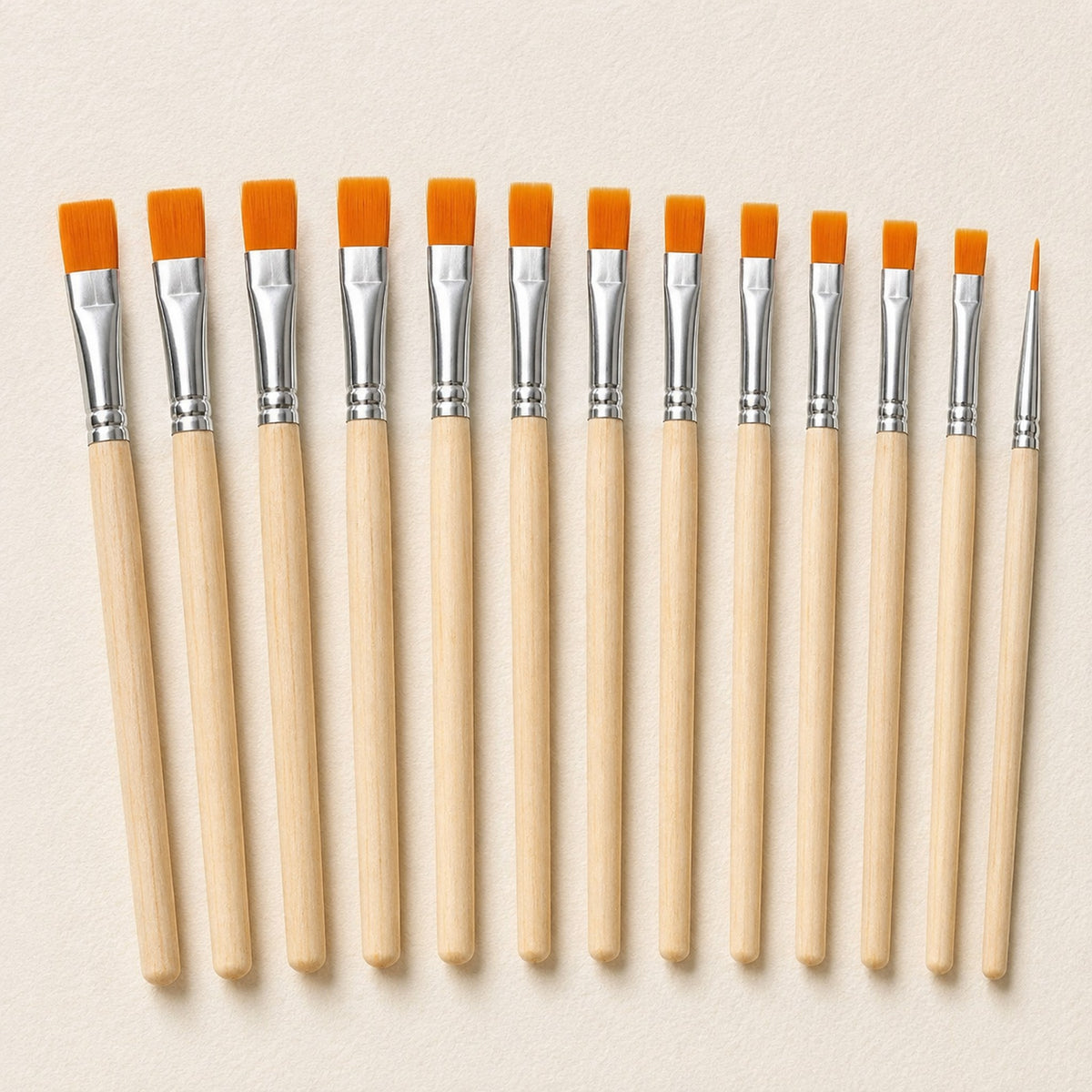 Close view of the thirteen brush heads on warm ivory, showing the flat orange filament tips stepping down in width and the single fine liner at the end.