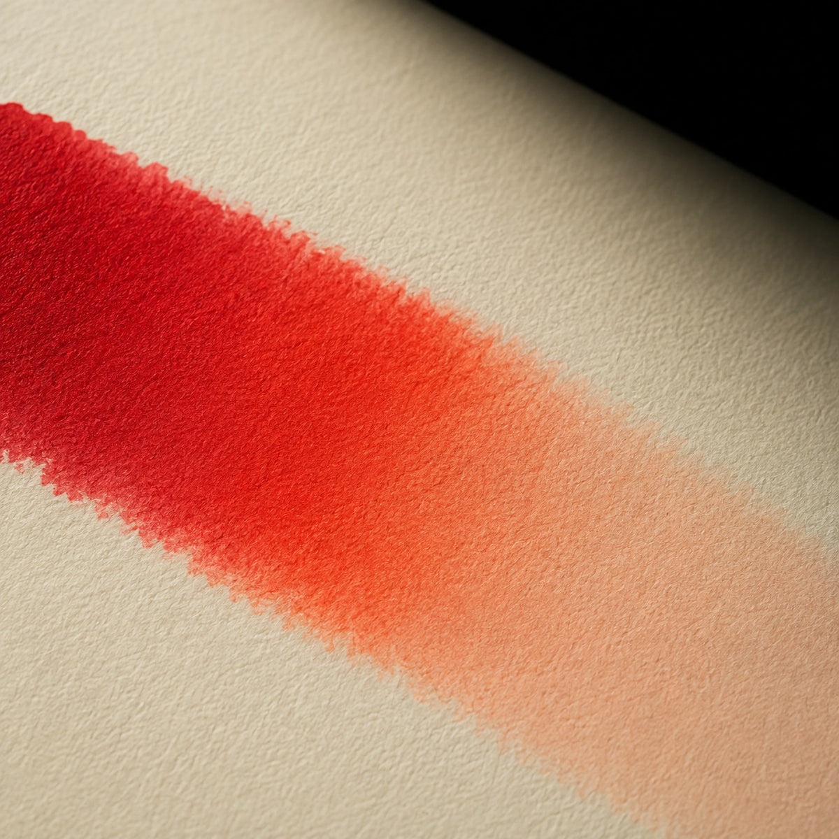 Close macro of alcohol ink blending from deep red through vermilion into soft peach on ivory art paper