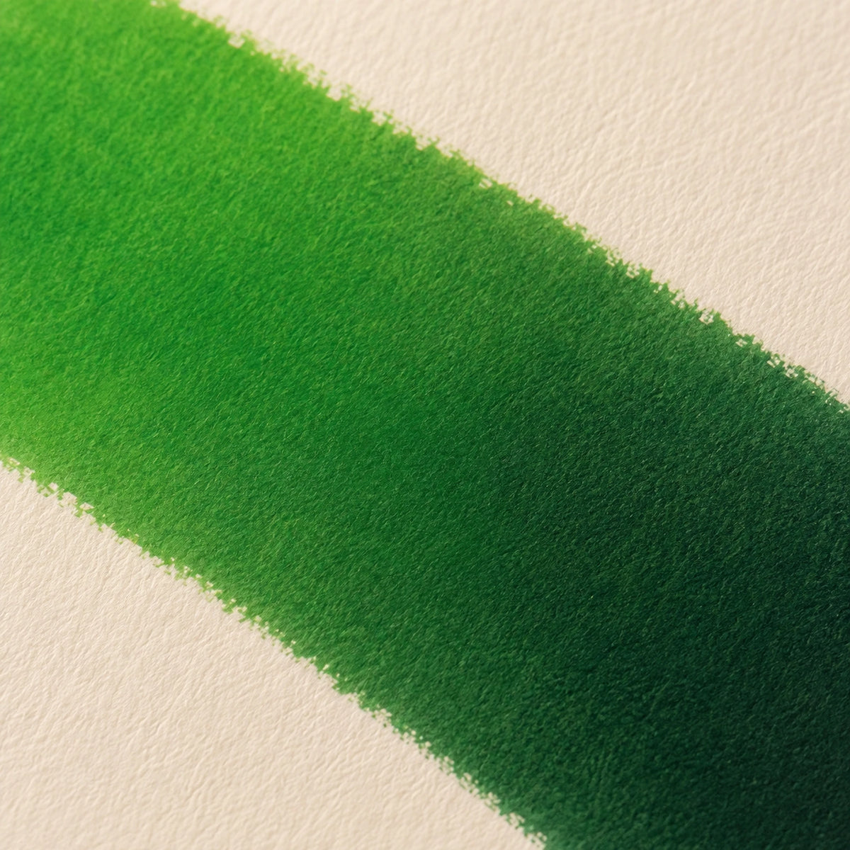 Close macro of alcohol ink blending from bright leaf green into deep forest green on ivory art paper