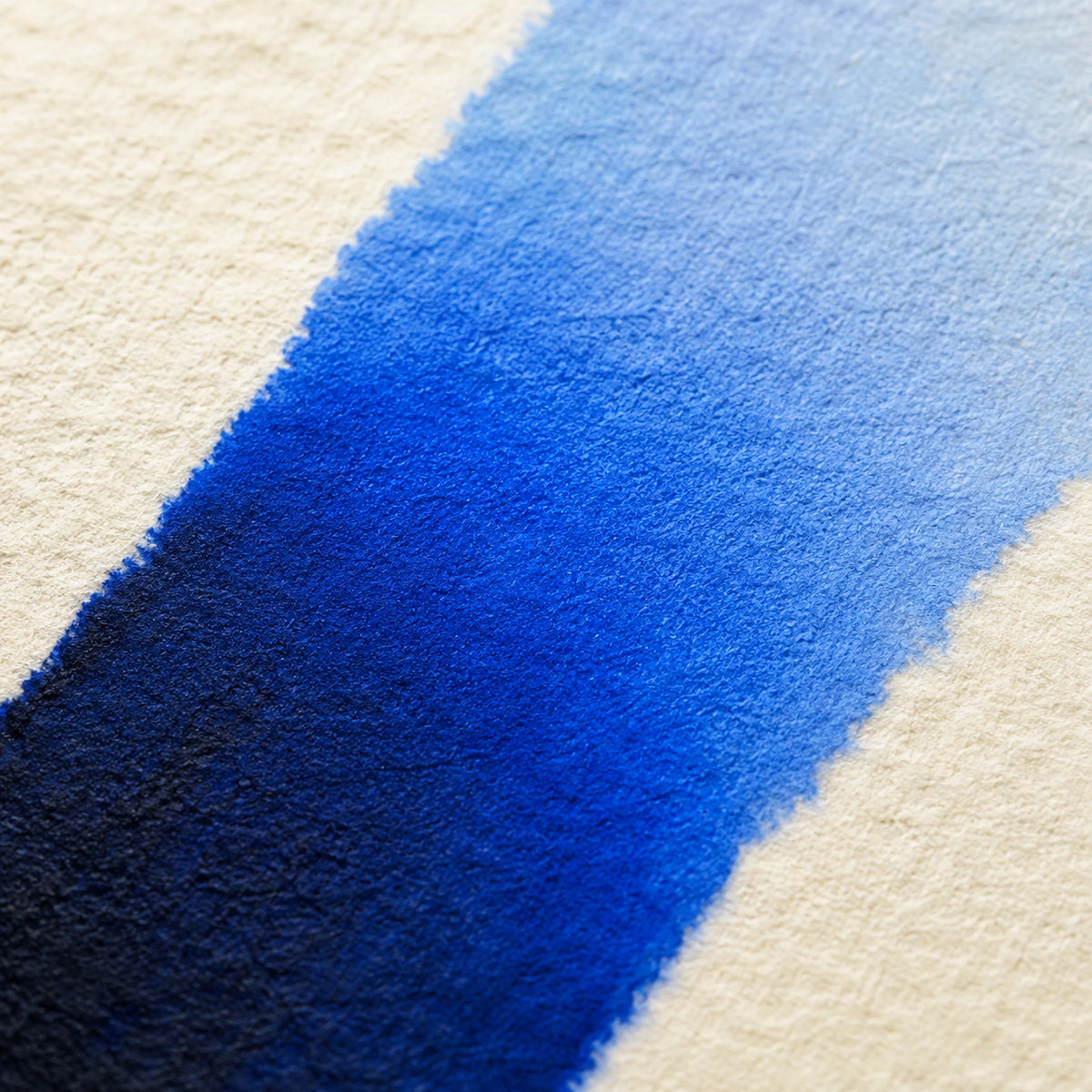 Close macro of alcohol ink blending from deep navy through royal blue into pale sky blue on ivory paper